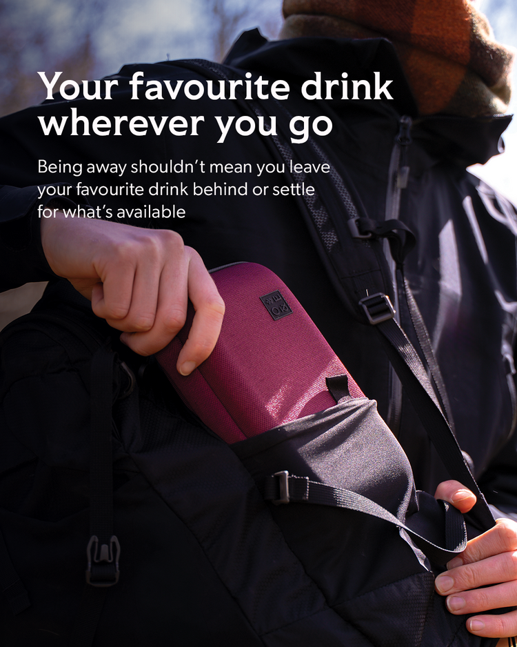 A close-up lifestyle shot of a person wearing a black backpack and winter jacket, holding a burgundy insulated travel mug in the side pocket. The image features promotional text in white on the left side.